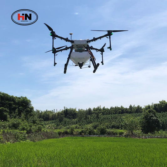 Agricultural sprayer drone hovering, four propellers and white spray tank visible.